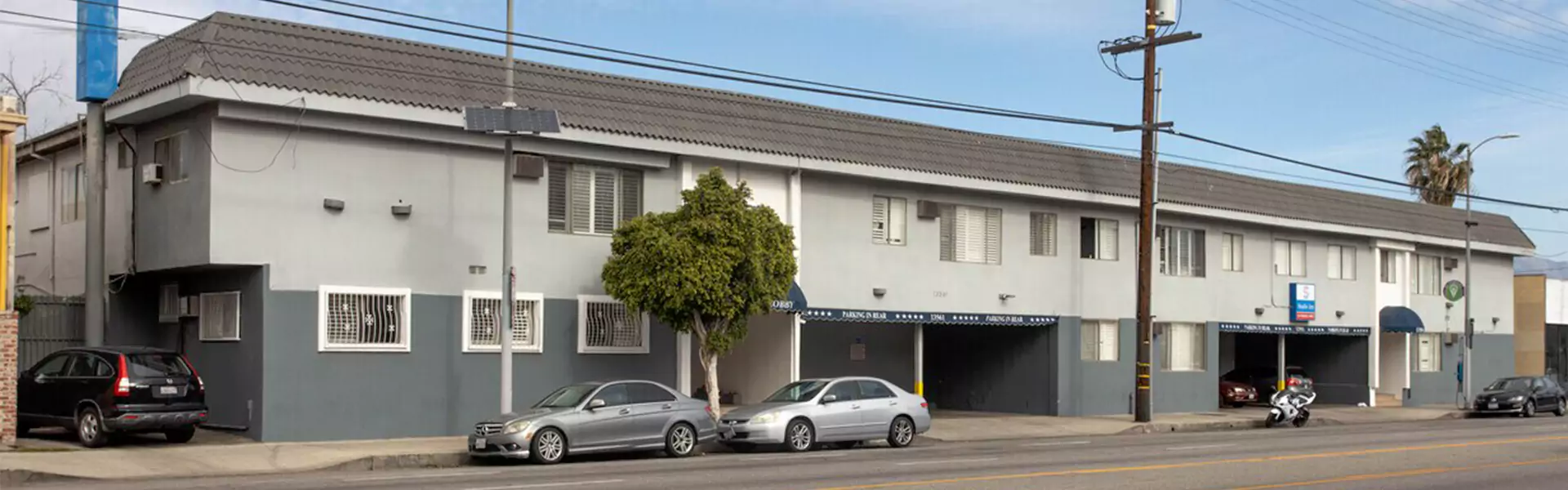 Gray apartment building with parking area and trees.