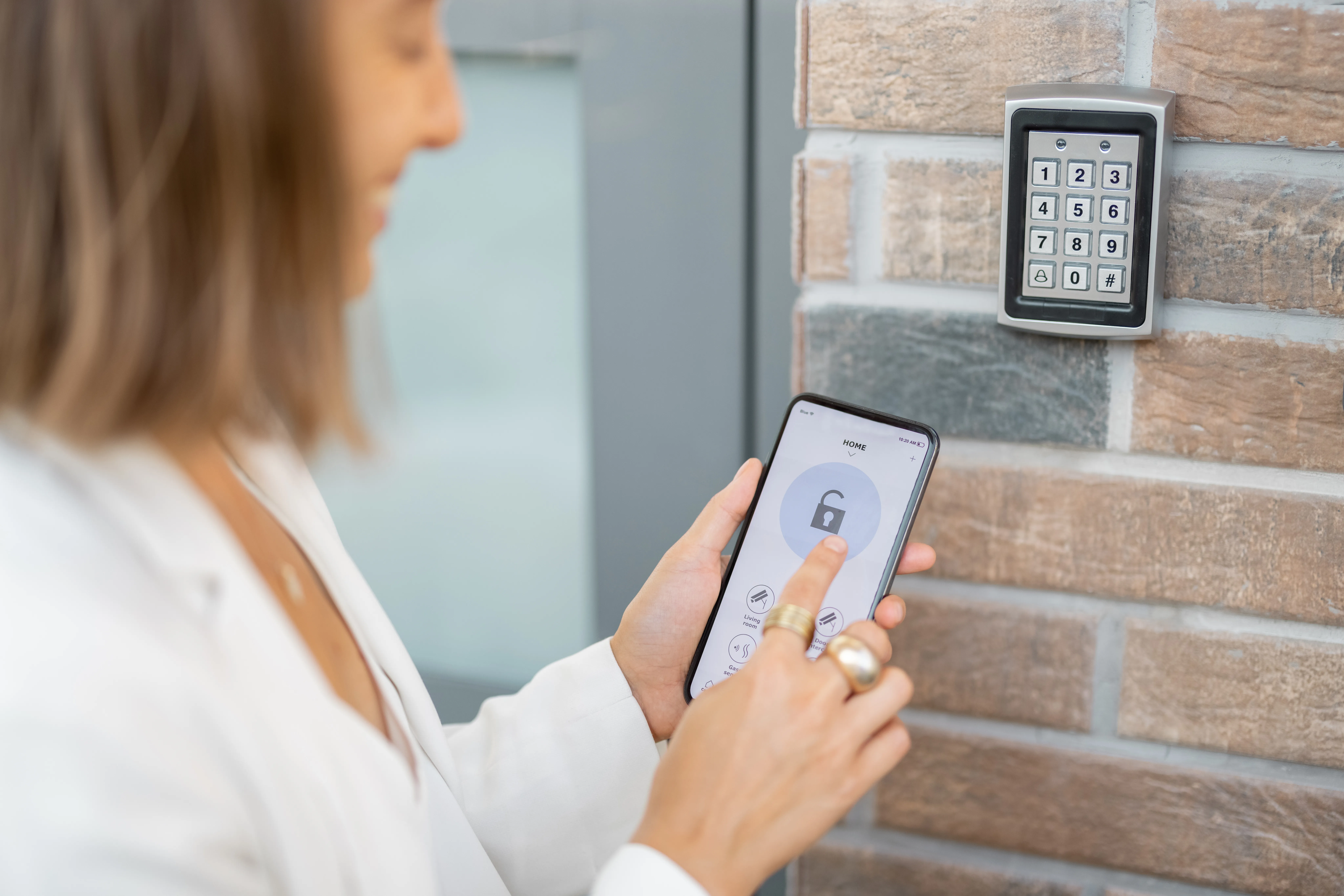 Person using smartphone to unlock door keypad.