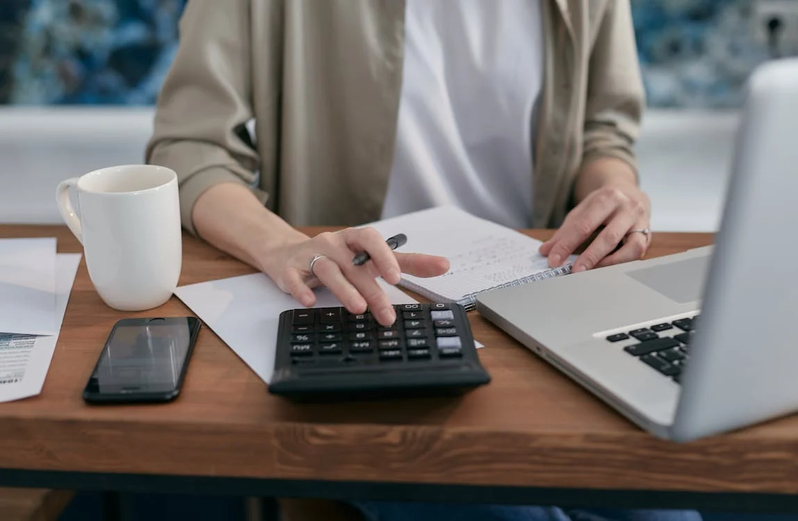 someone using a computer/phone while also using a notepad/calculator; a portrayal of budgeting that involves a computer