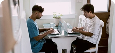 Two friends working on laptops at a table.